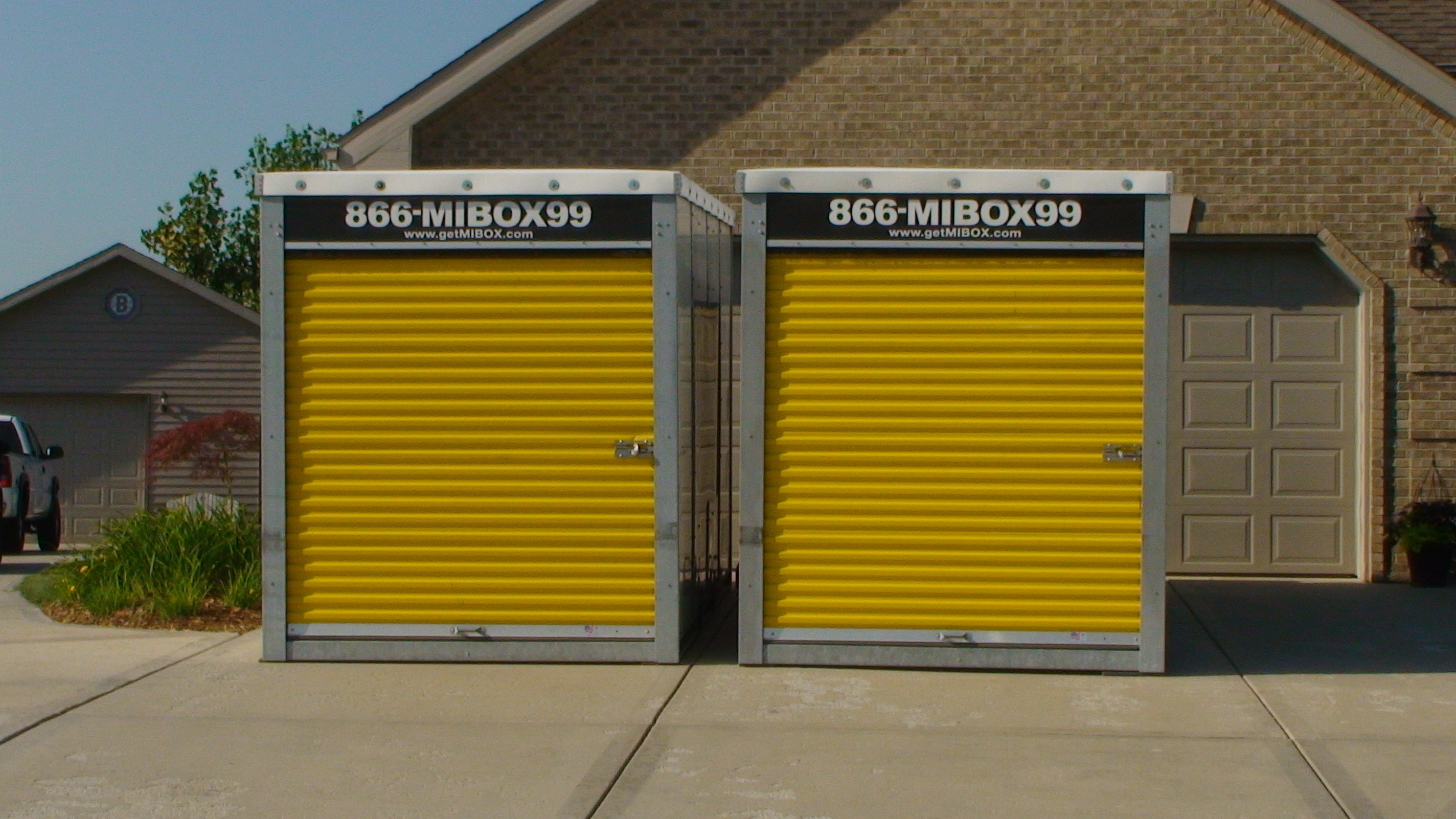 Two MI-BOX portable storage containers side-by-side in a driveway